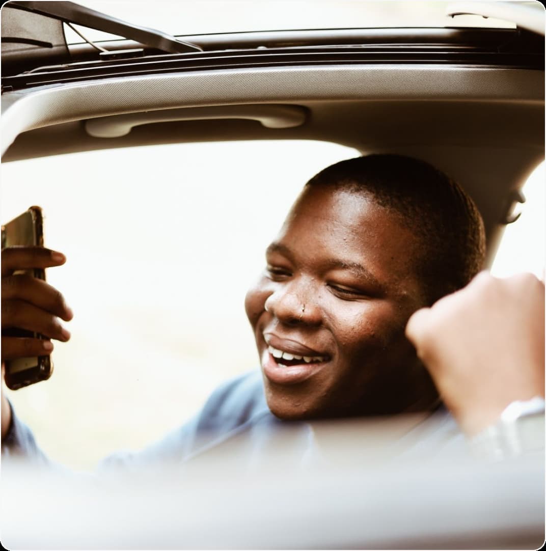 A commuter smiling at their phone while leaning out of a car window